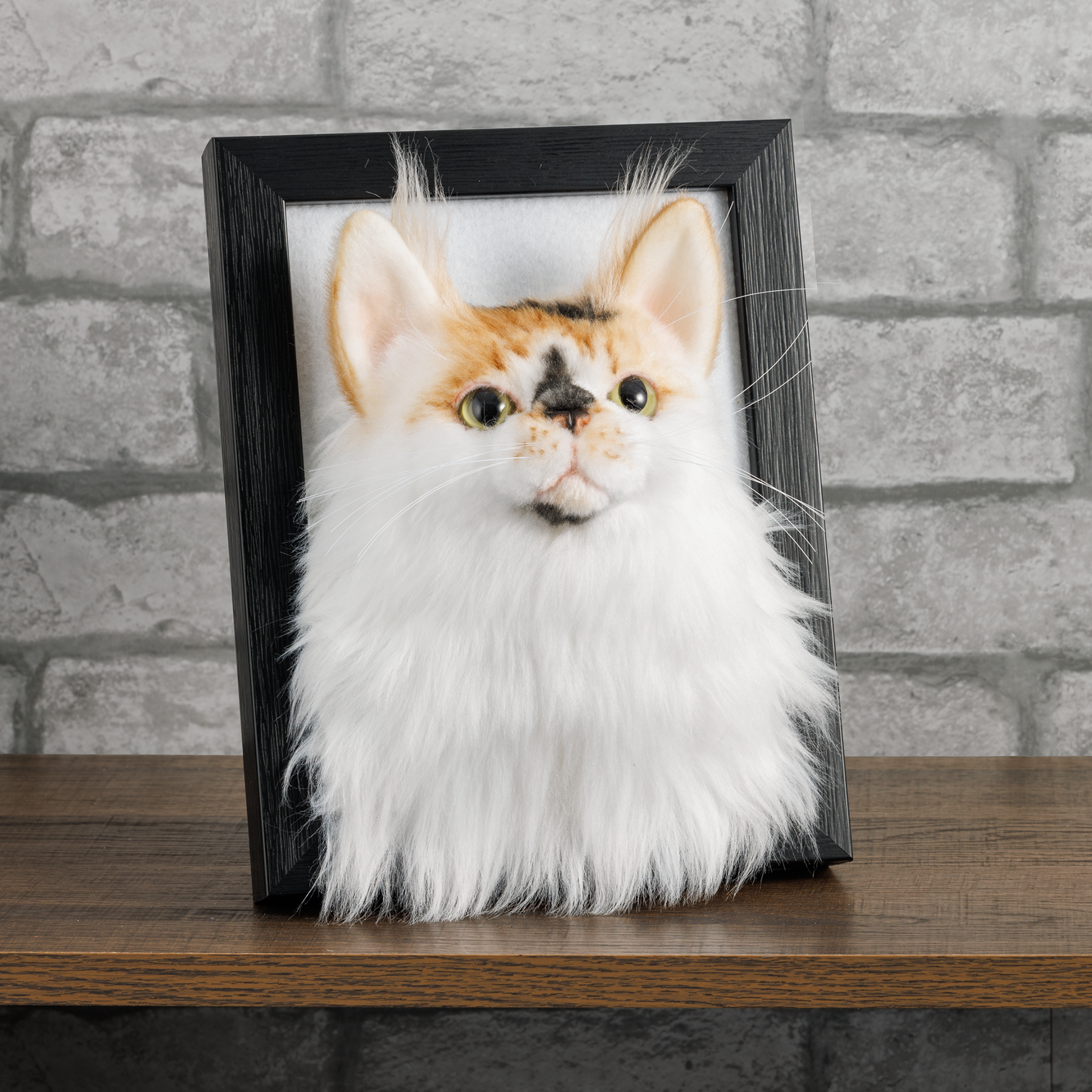Custom pet portrait of orange and white cat with green eyes in black wooden frame against brick wall background