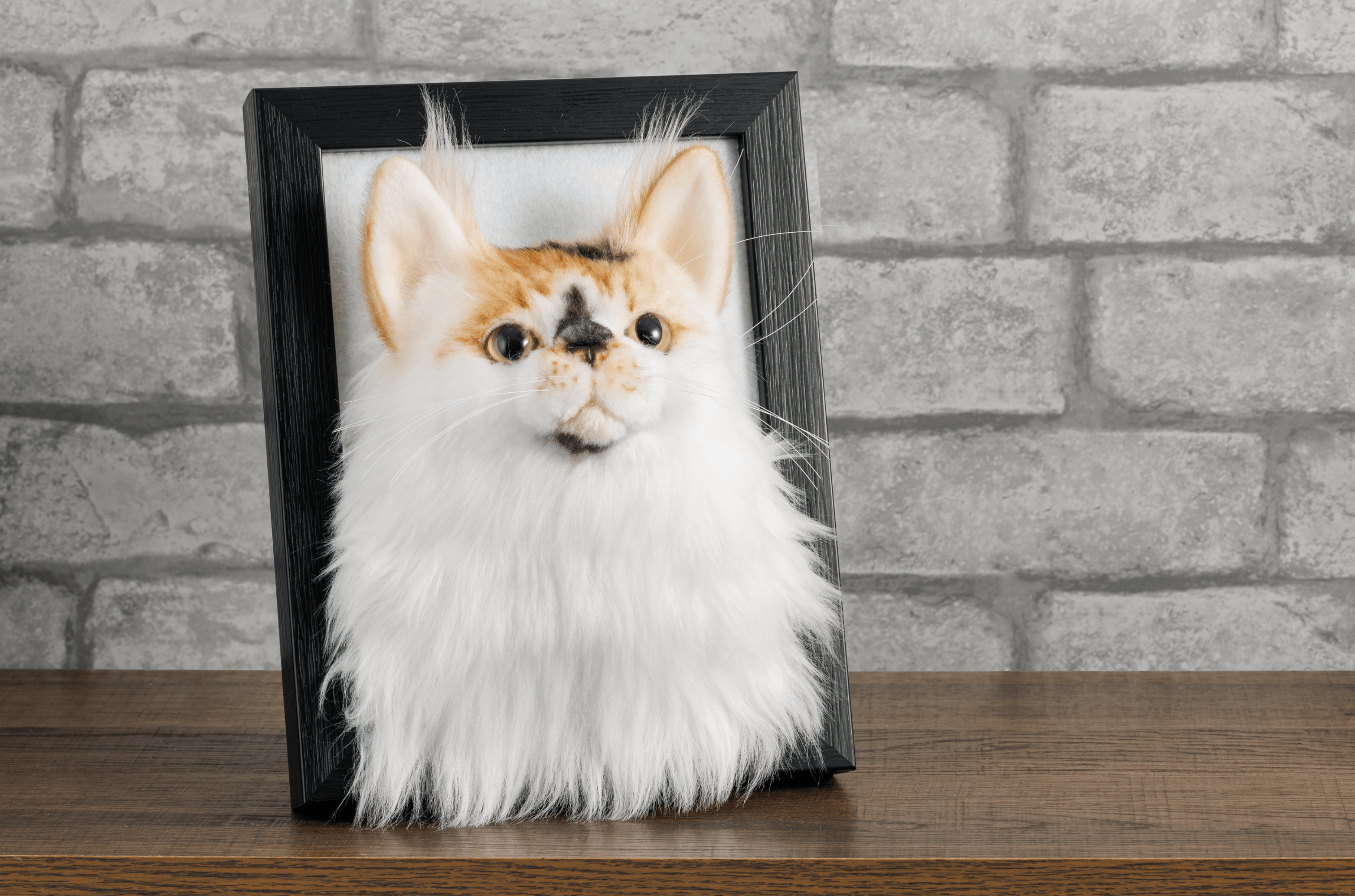 Custom pet portrait of orange and white cat with green eyes in black wooden frame against brick wall background