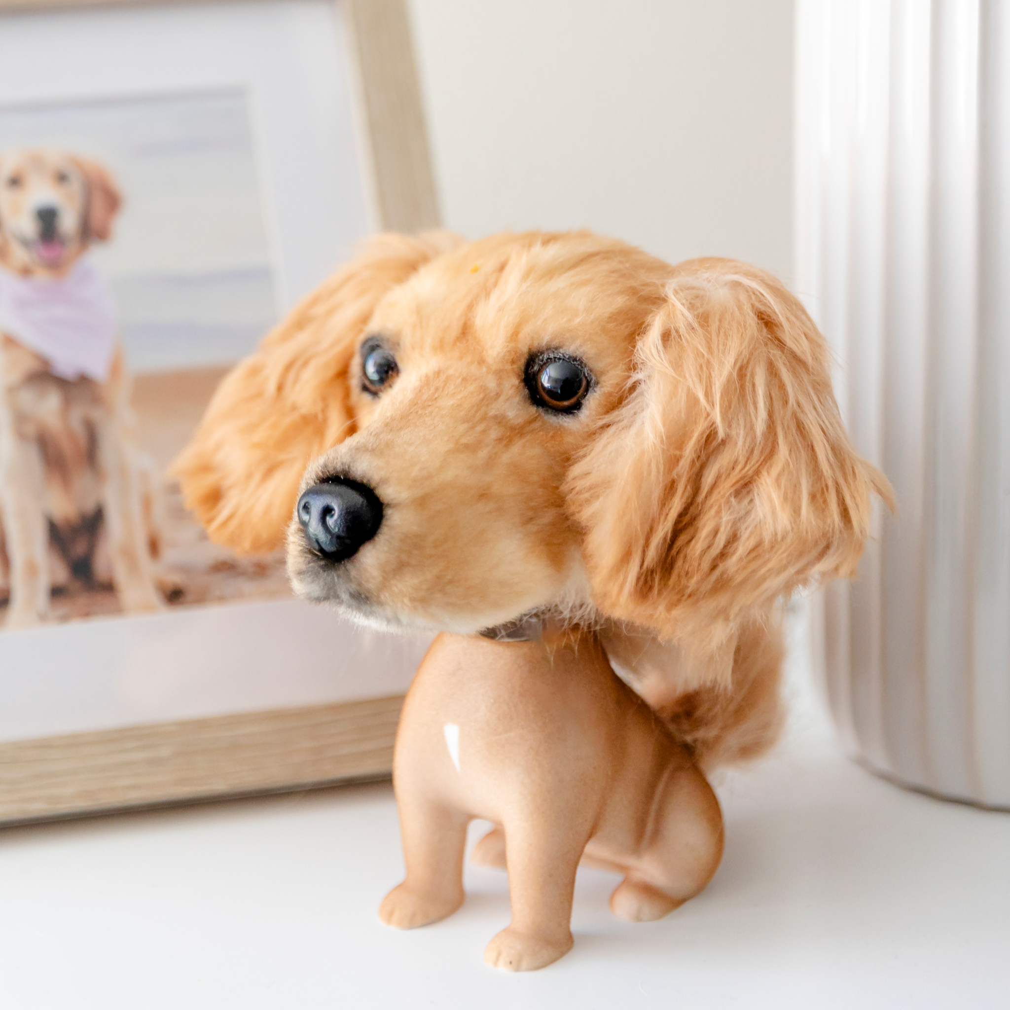 Golden Retriever bobblehead on dark surface beside framed photo of dog at the beach.
