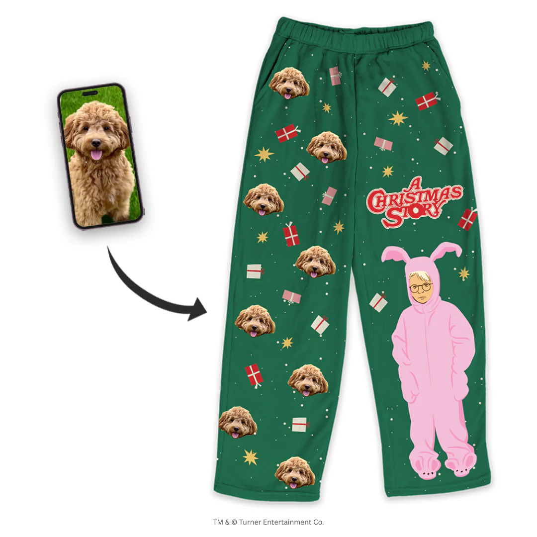 A pair of green pajama pants, patterned with gifts and starbursts, features a graphic of Ralphie from A Christmas Story in the pink bunny suit, along with the movie title. The pants are customized with a repeating design of a fluffy brown Cockapoo's face.