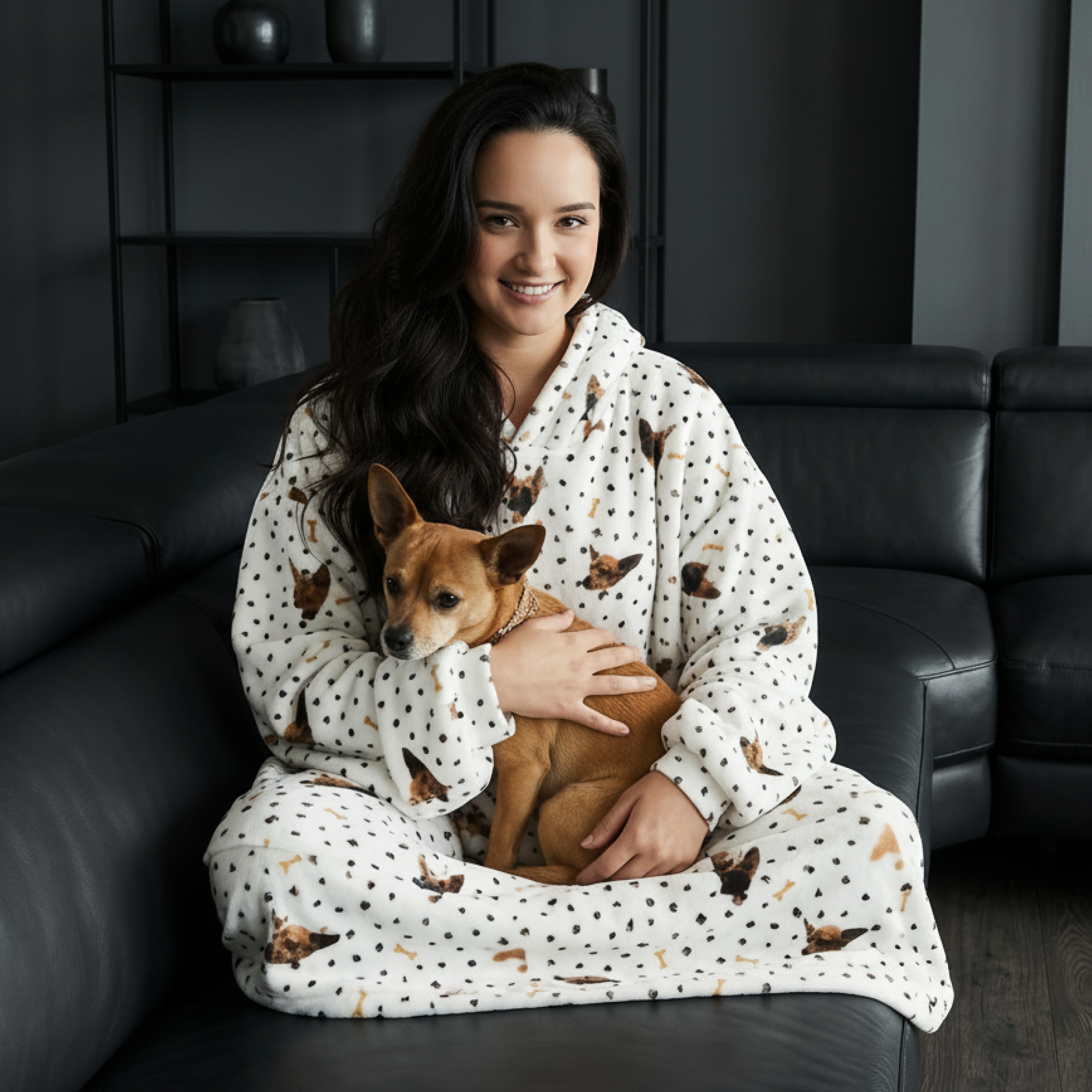 Person in pajamas holding a small dog on a couch.