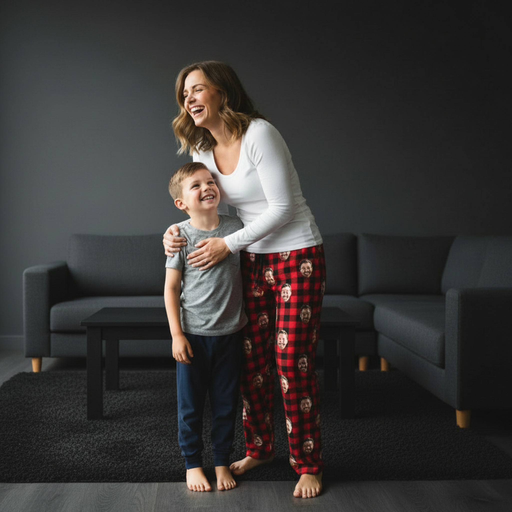 Mom and son laughing together in a dark-toned living room, wearing face-print pajamas.