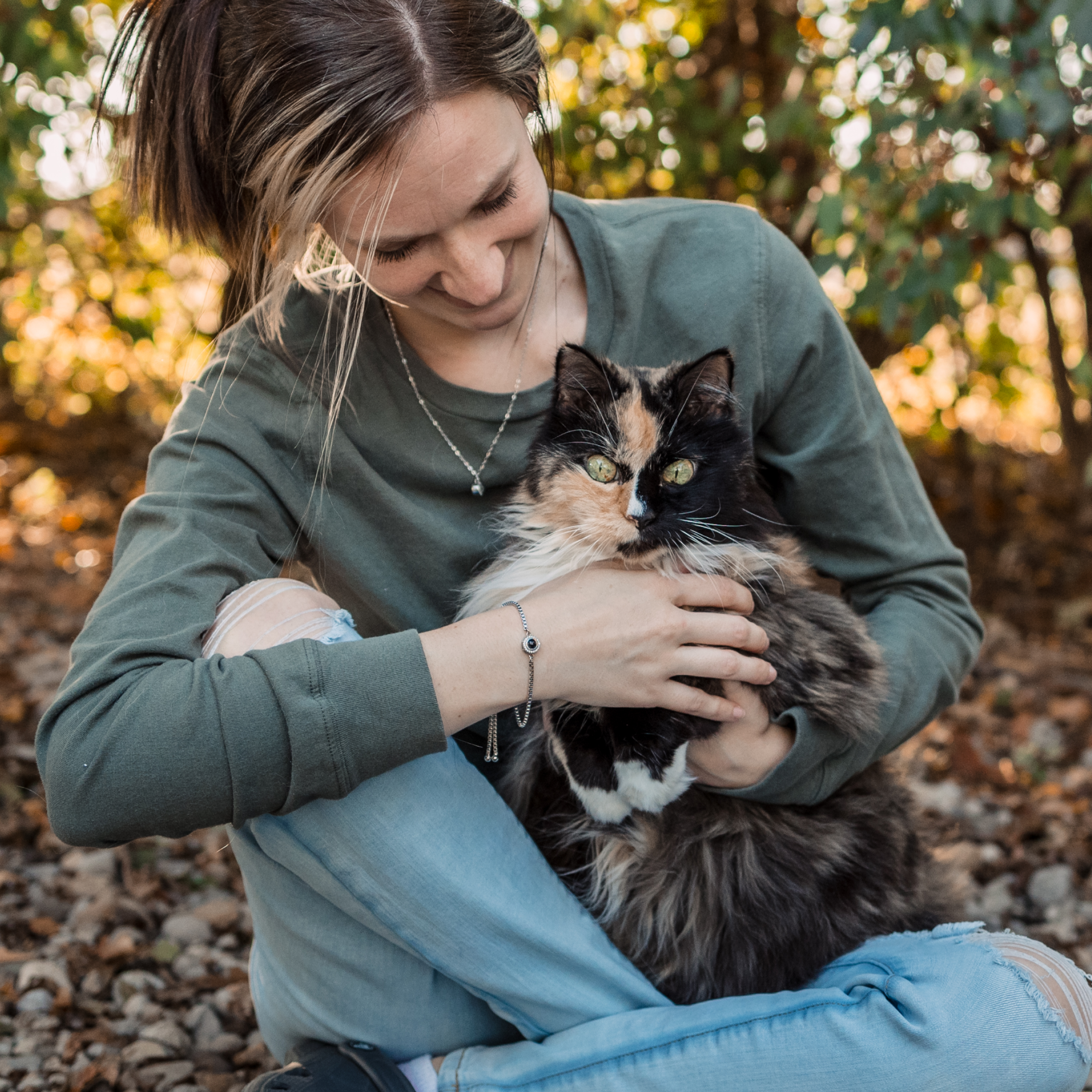 he woman is wearing a sage green sweatshirt and a silver chain bracelet that features a small, circular black-and-silver charm (likely a projection pendant). 