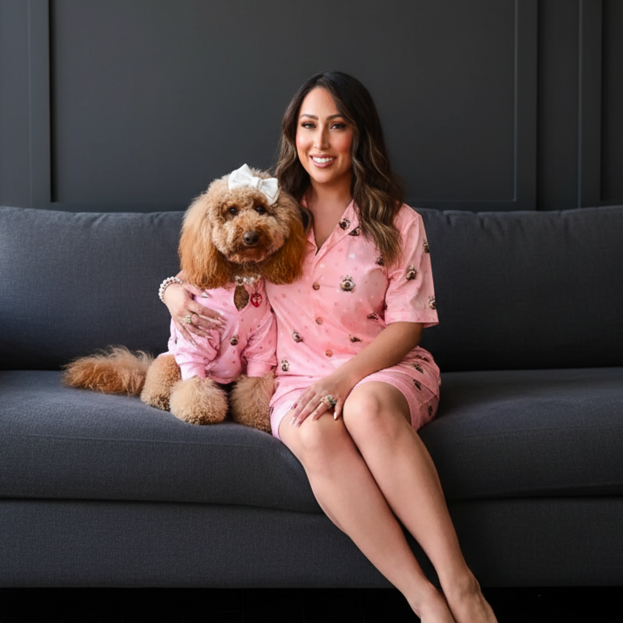 Woman on outdoor steps with fluffy poodle-mix dog wearing matching pink dog-print pajamas