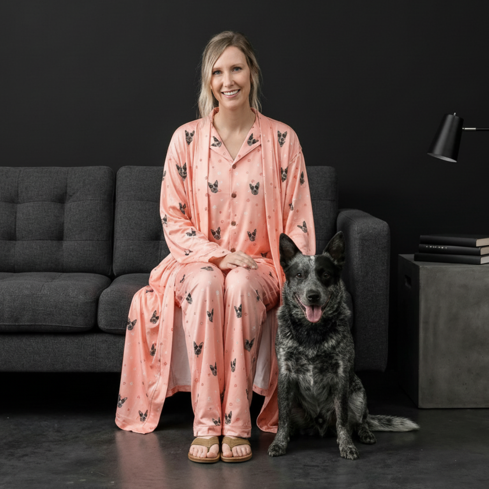 Woman in pink paw-print pajamas with a speckled dog sitting on a couch.