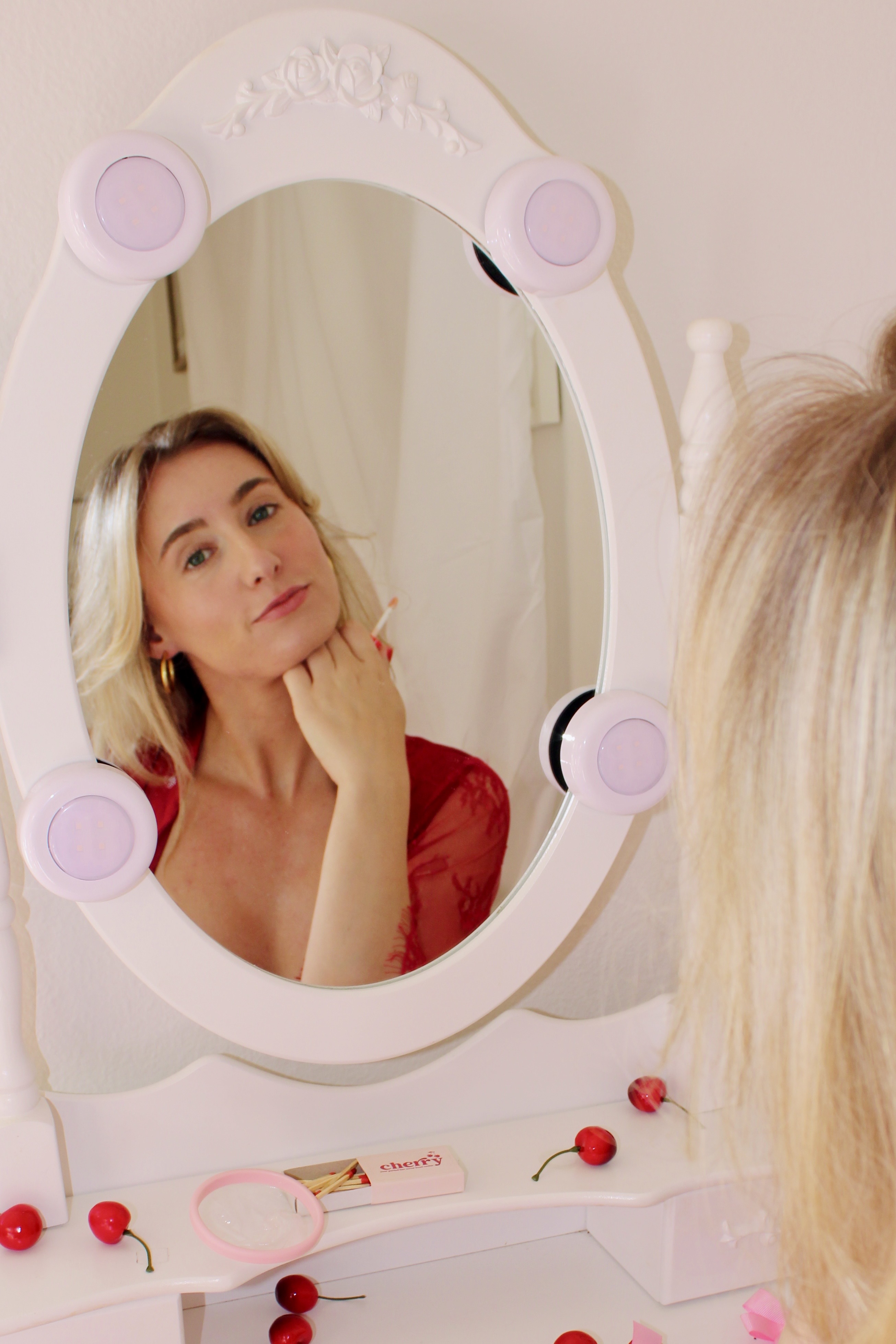 Person looking at their reflection in a white vanity mirror decorated with cherries.
