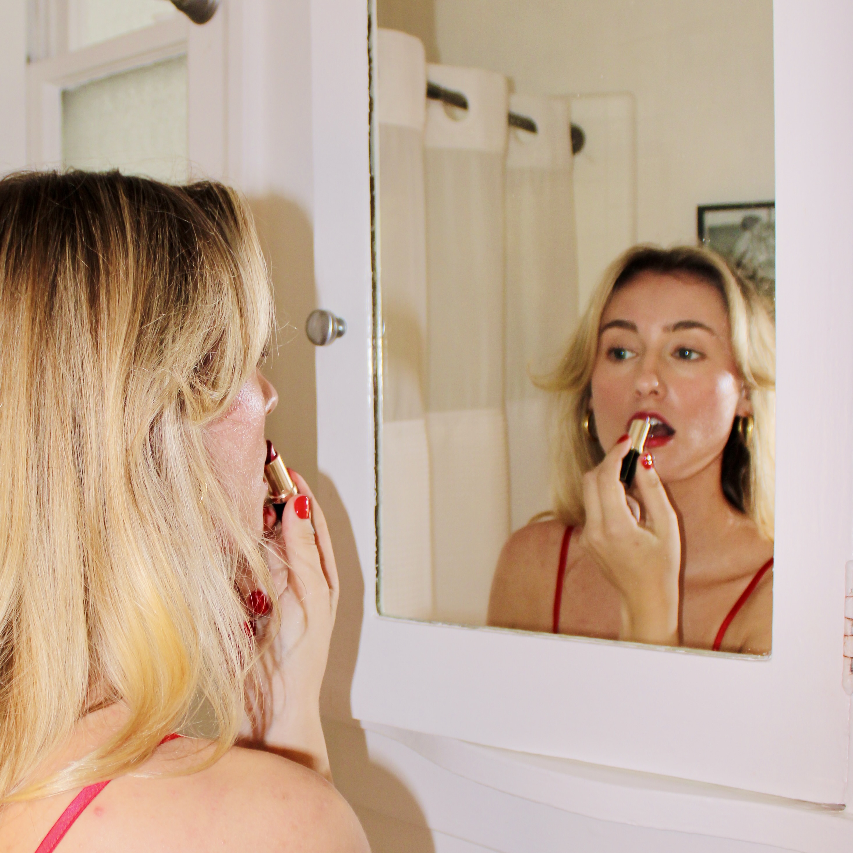 Woman applying lipstick in front of a bathroom mirror.