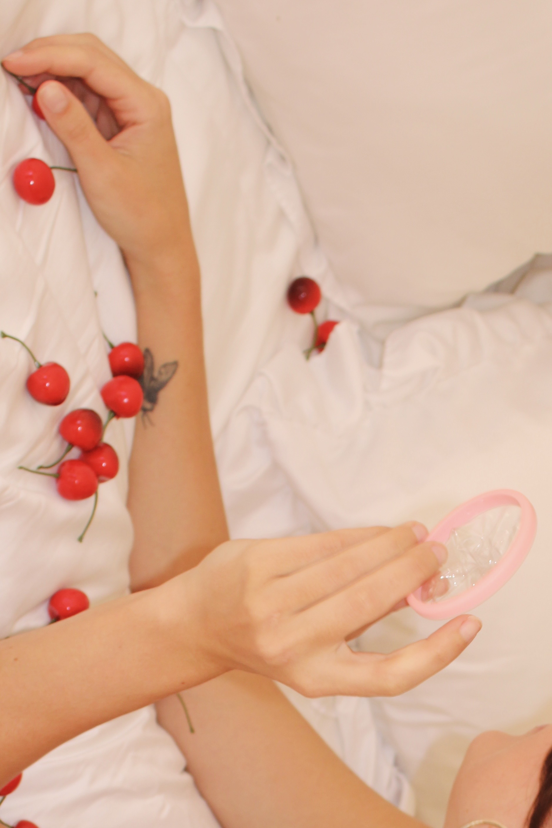 Hands holding cherries and a pink-bordered circular object on a white bed.