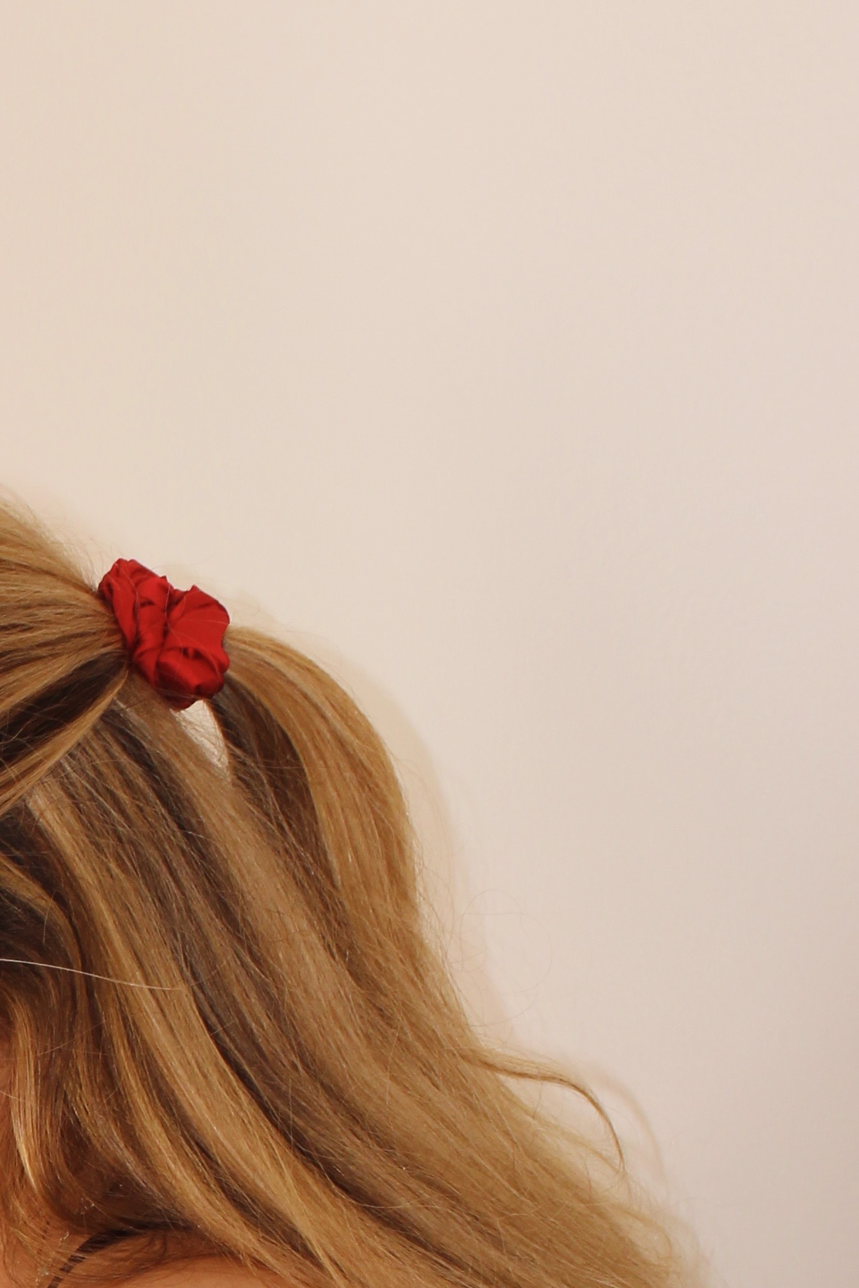 Close-up of hair with a red scrunchie on a plain background.