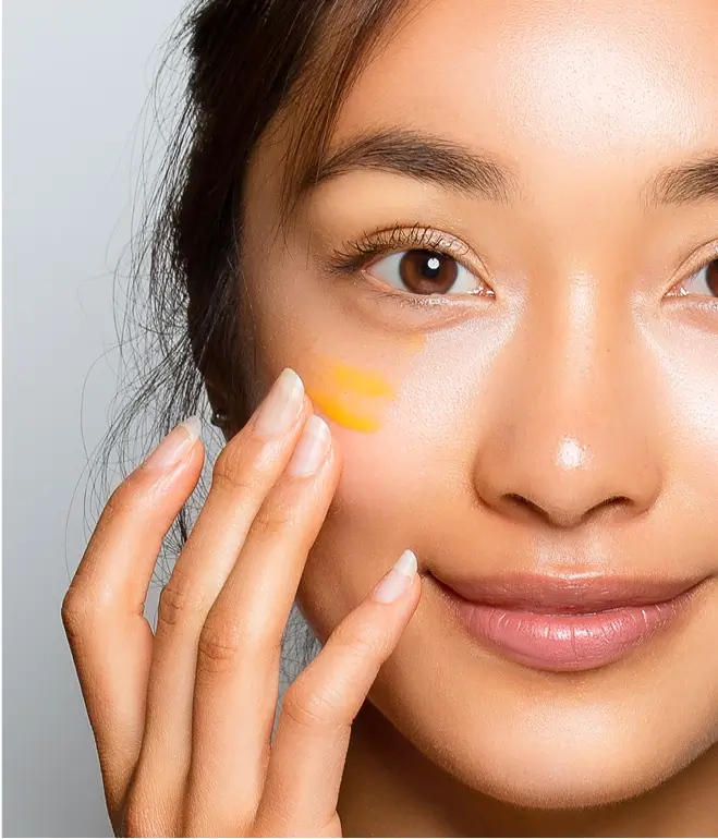 Person applying yellow cream to their cheek.