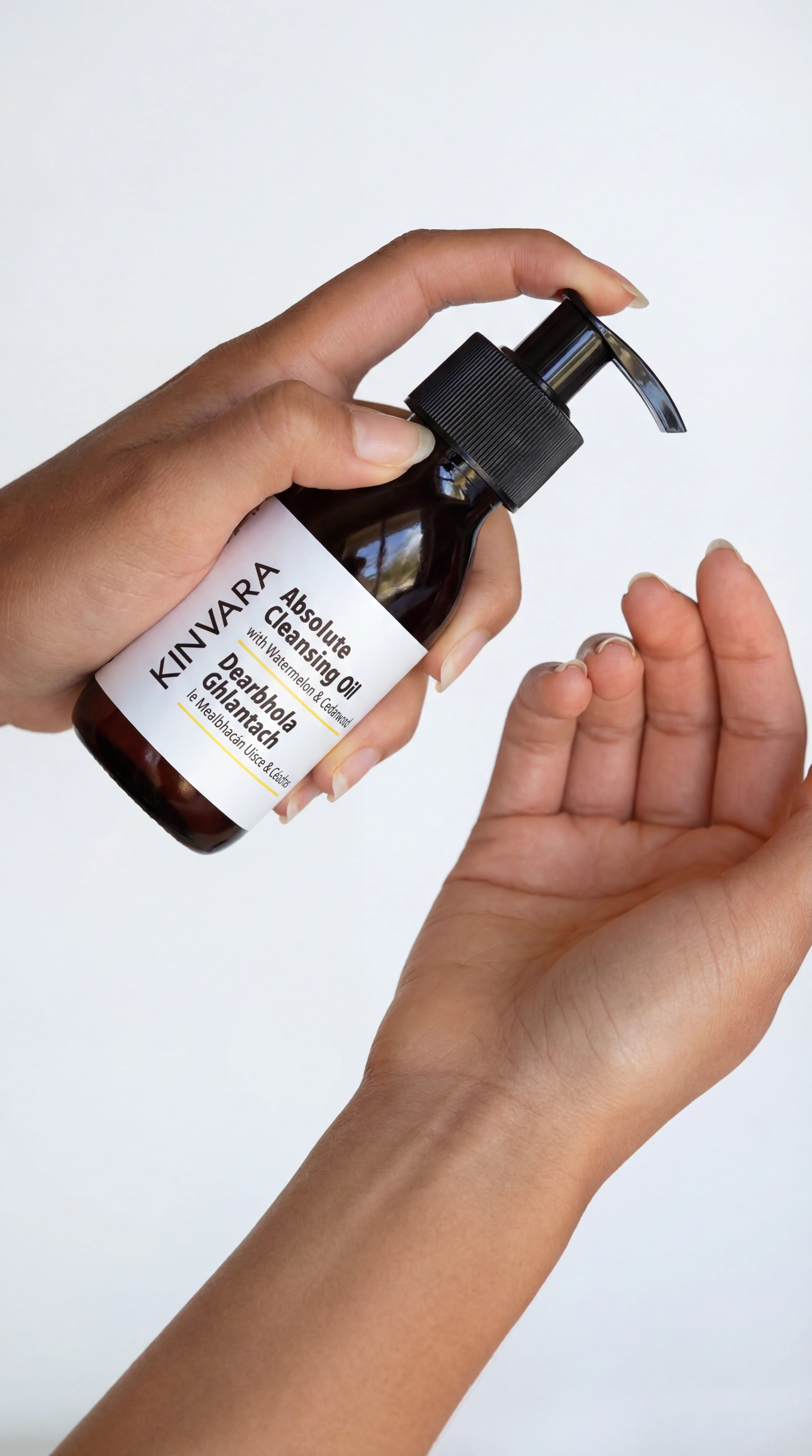 A person holds a bottle of Kinvara Absolute Cleansing Oil, preparing to dispense it into their hand.