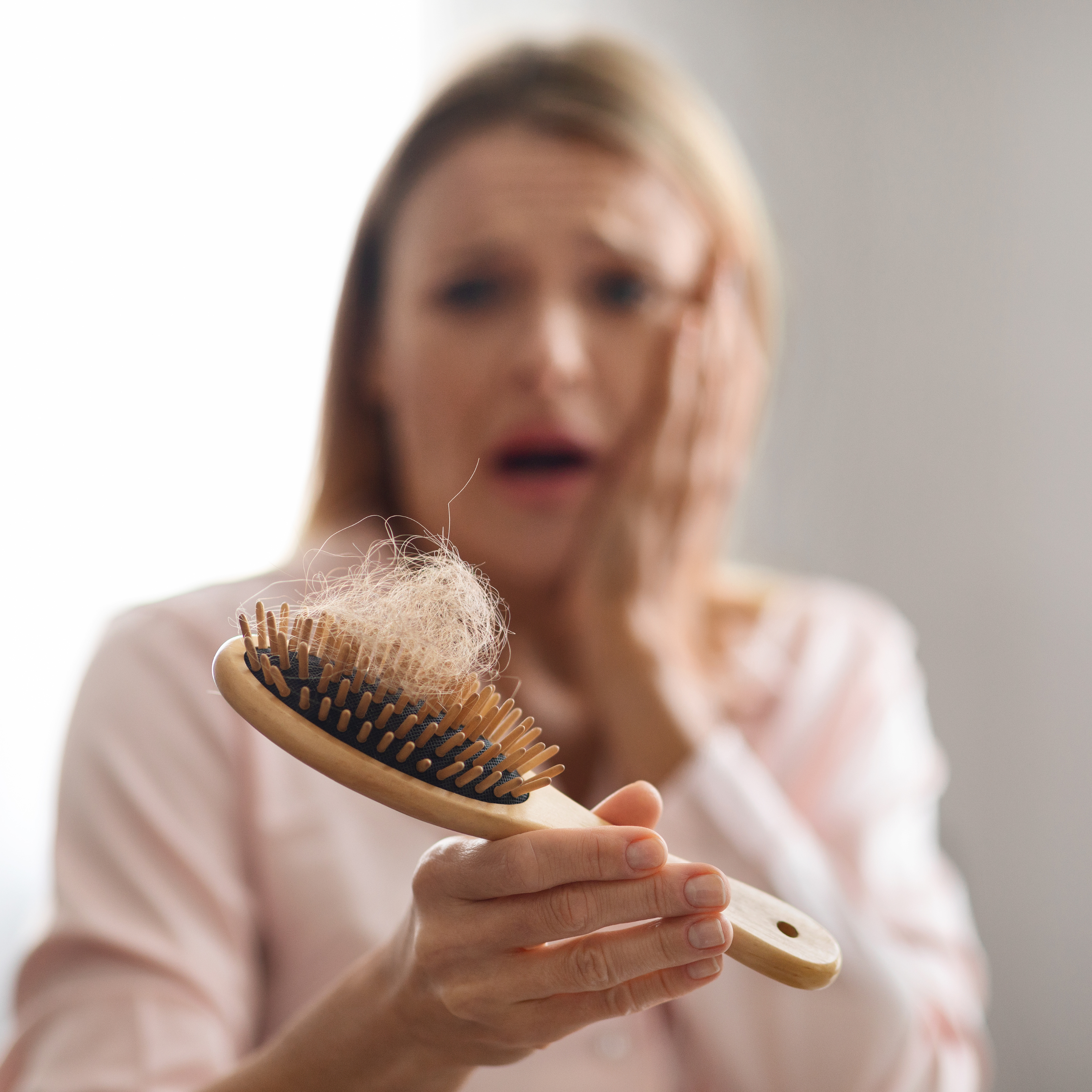 Woman holding a hairbrush with hair, looking concerned.