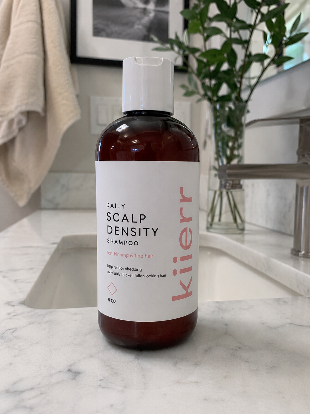 A bottle of Kiierr Daily Scalp Density Shampoo rests on a white marble bathroom counter.