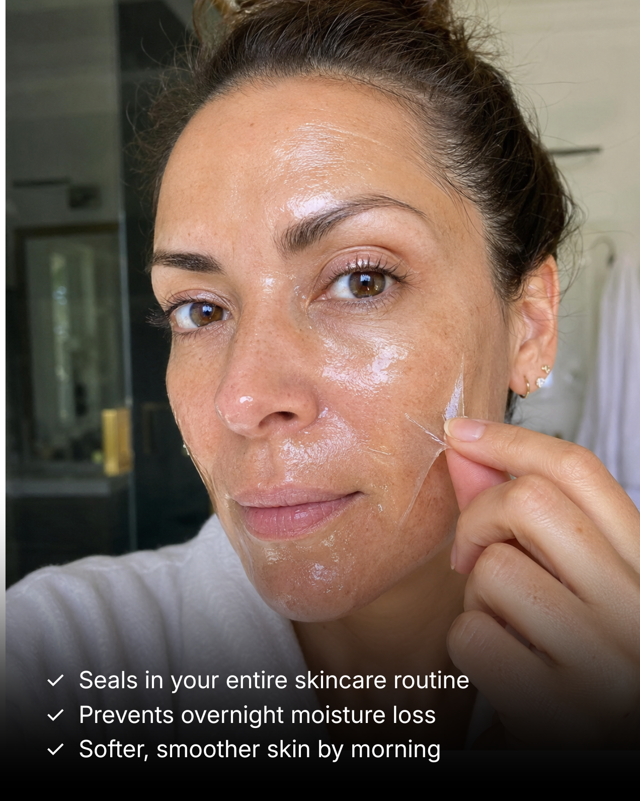 A woman in a white robe peeling a clear, transparent mask off her cheek.
