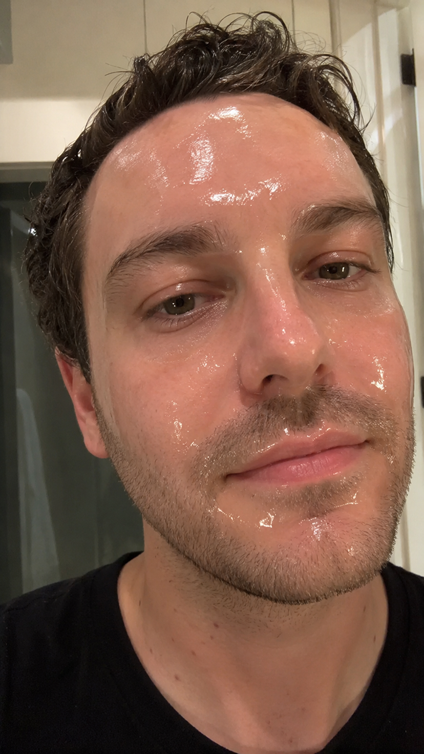 A close-up selfie of a man with a clear, shiny face mask applied to his skin.