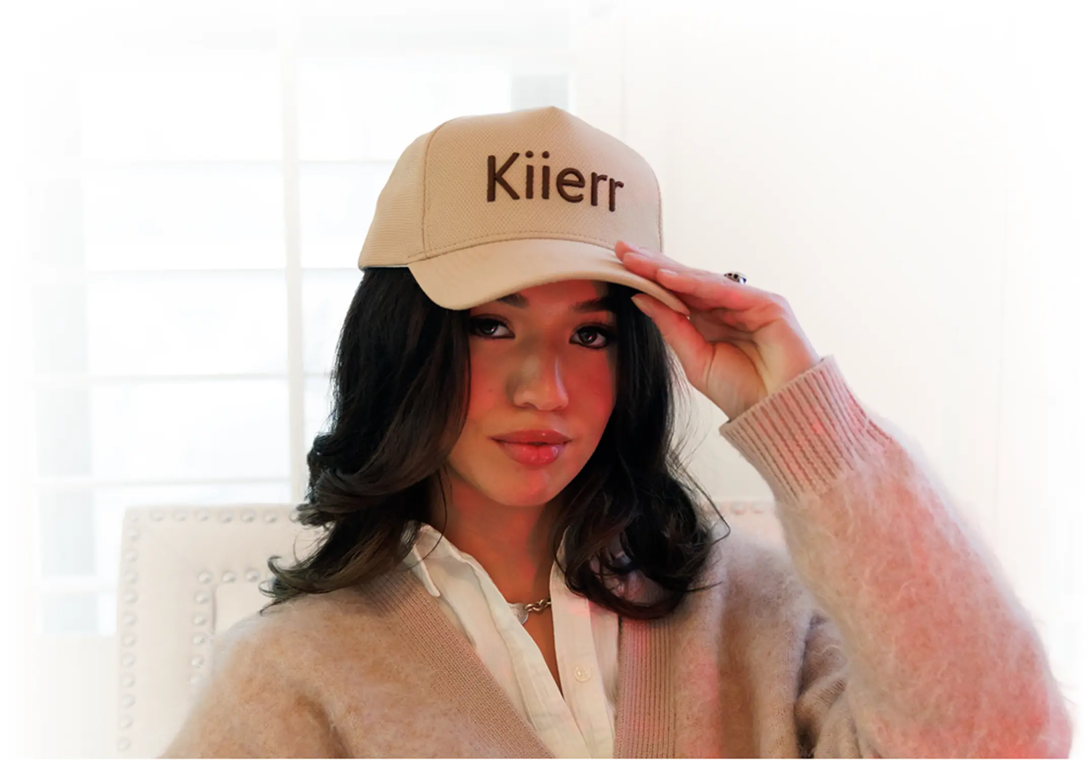 A woman with dark hair wearing a beige baseball cap with the word 'Kiierr' on it.