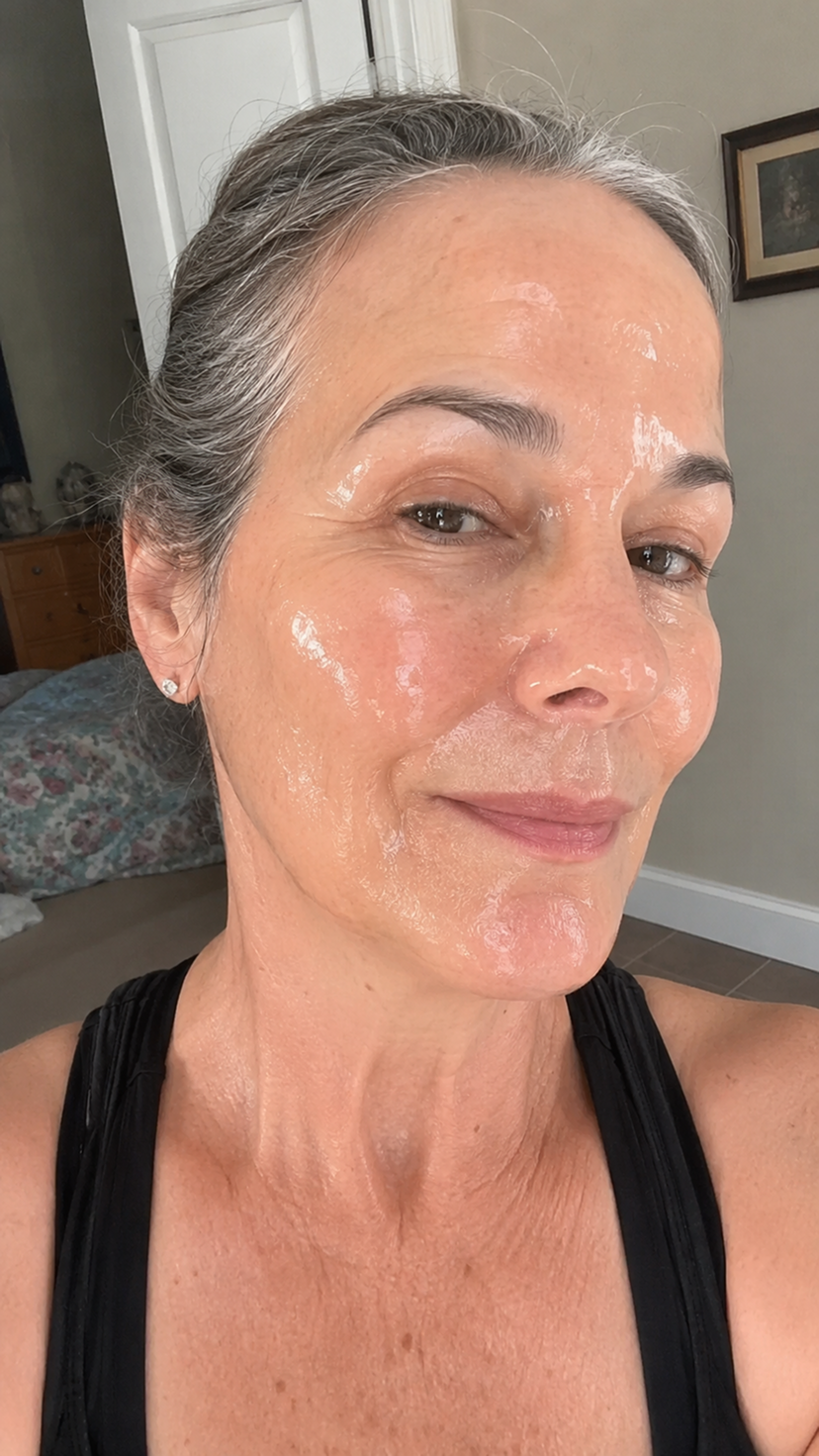 A close-up of a woman with a shiny skincare product applied to her face and neck.