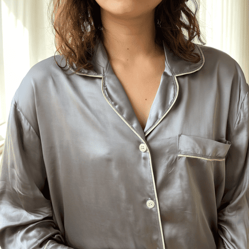 Person wearing a gray satin pajama top with white piping.