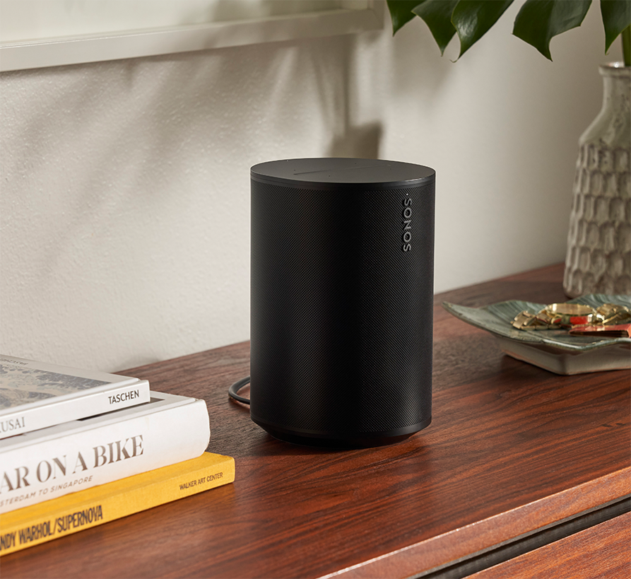 Black Sonos speaker on a wooden table with books and a decorative tray.