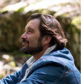 Man in a denim jacket looking upwards, outdoors.