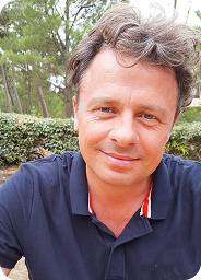 Person smiling outdoors with trees in the background.
