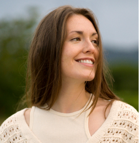 Smiling person with long hair in a natural outdoor setting.