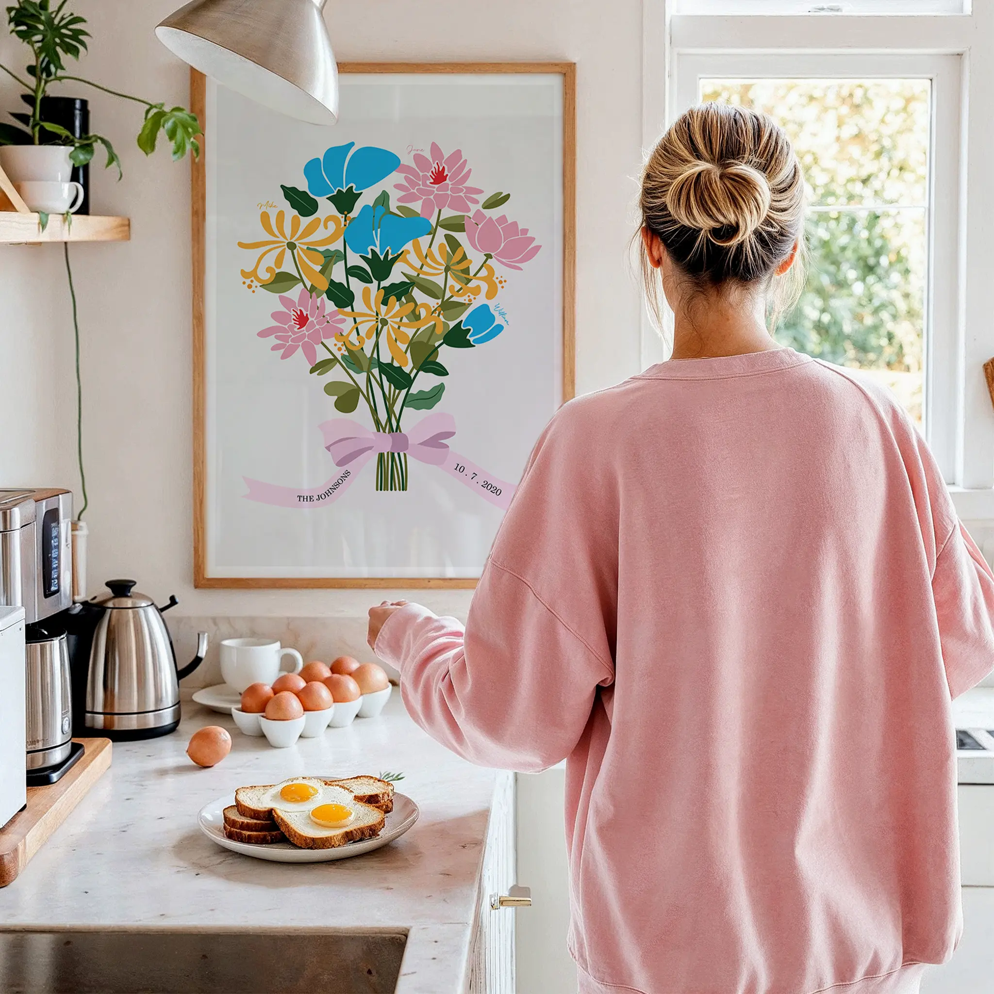 Person in pink sweater in kitchen, viewing floral artwork on wall.