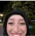 A person in a hoodie smiling outdoors at night.