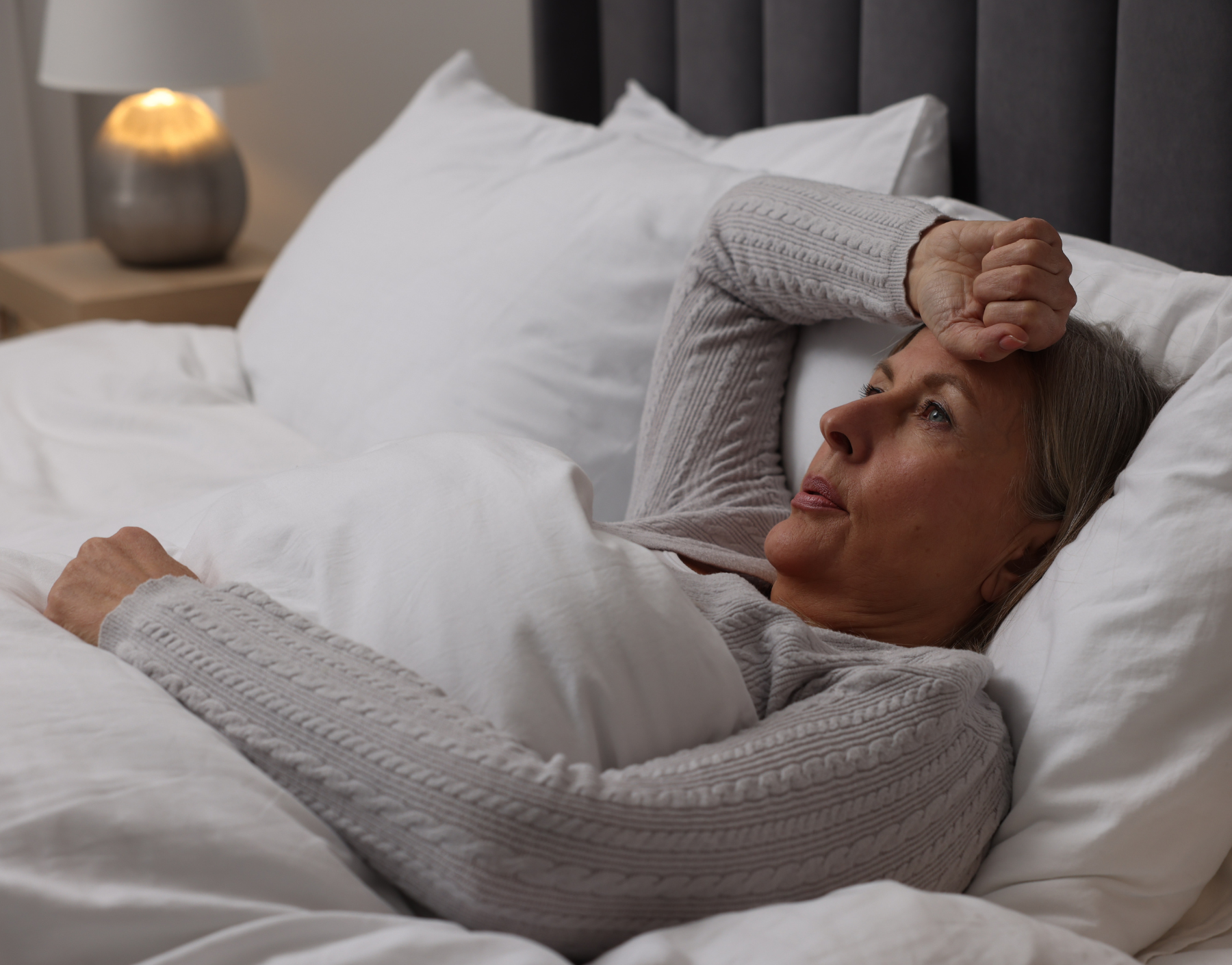 Woman lying in bed, looking thoughtful, with hand on forehead.