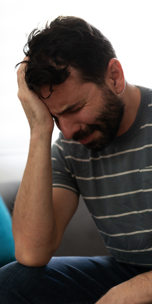 Man in striped shirt holding head, appearing distressed.