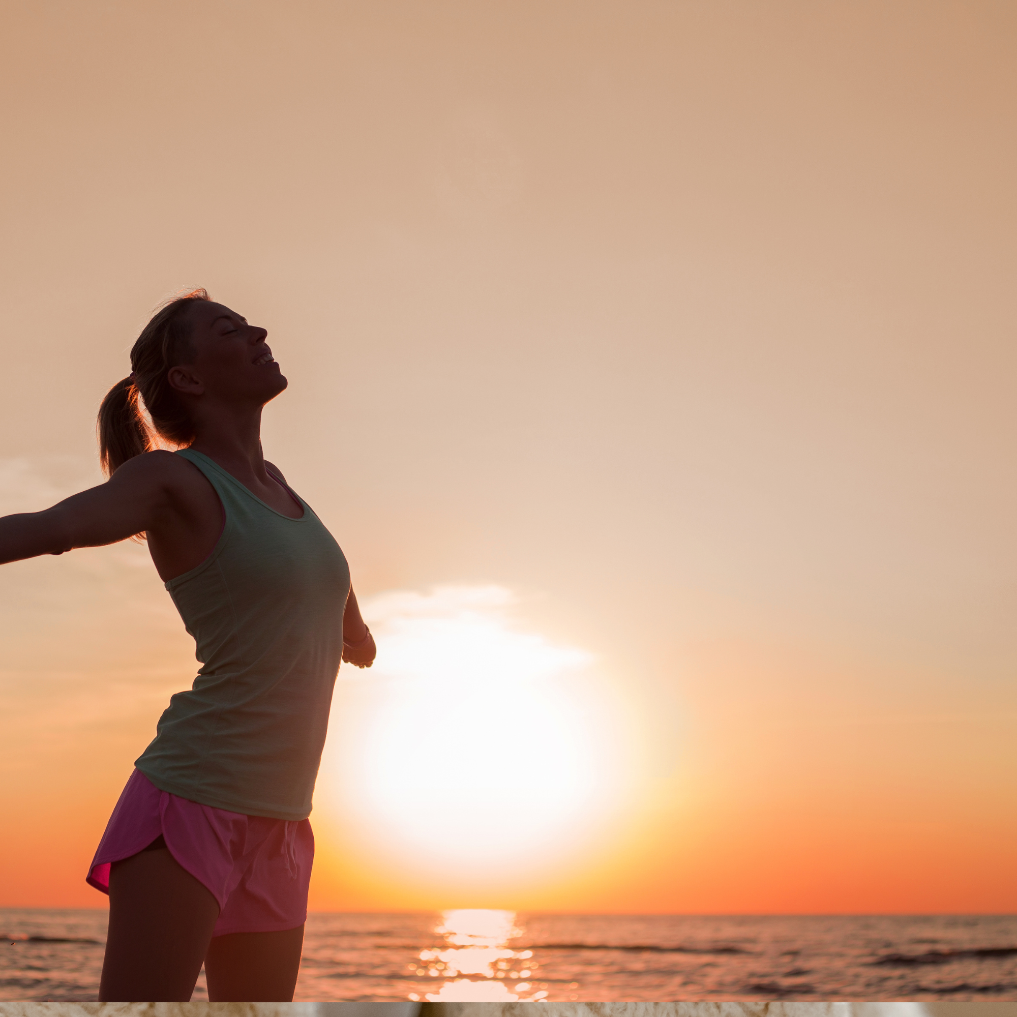 Silhouette of a woman with arms outstretched against a sunset over the ocean.