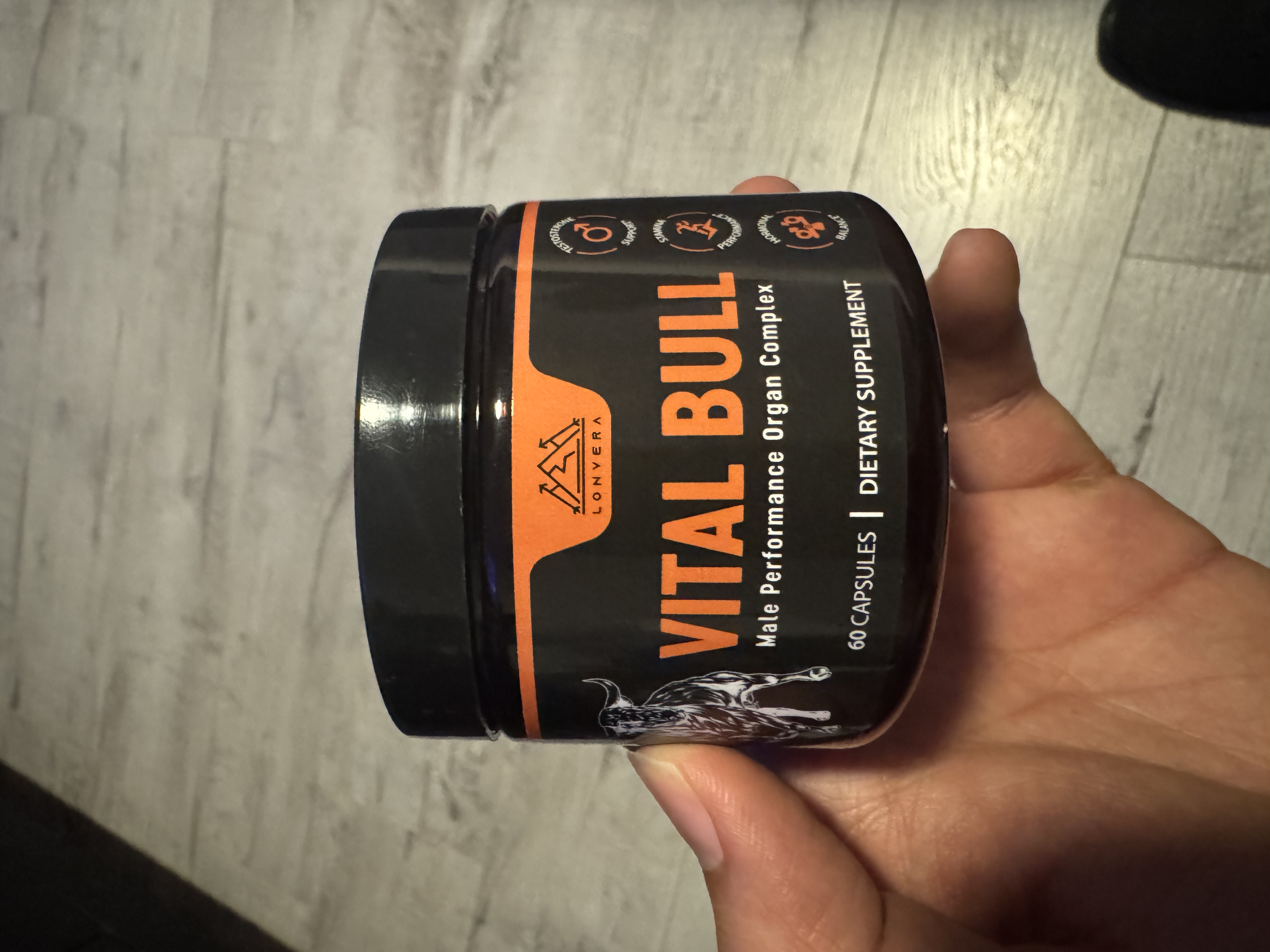 Hand holding a jar labeled 'Vital Bull' dietary supplement.
