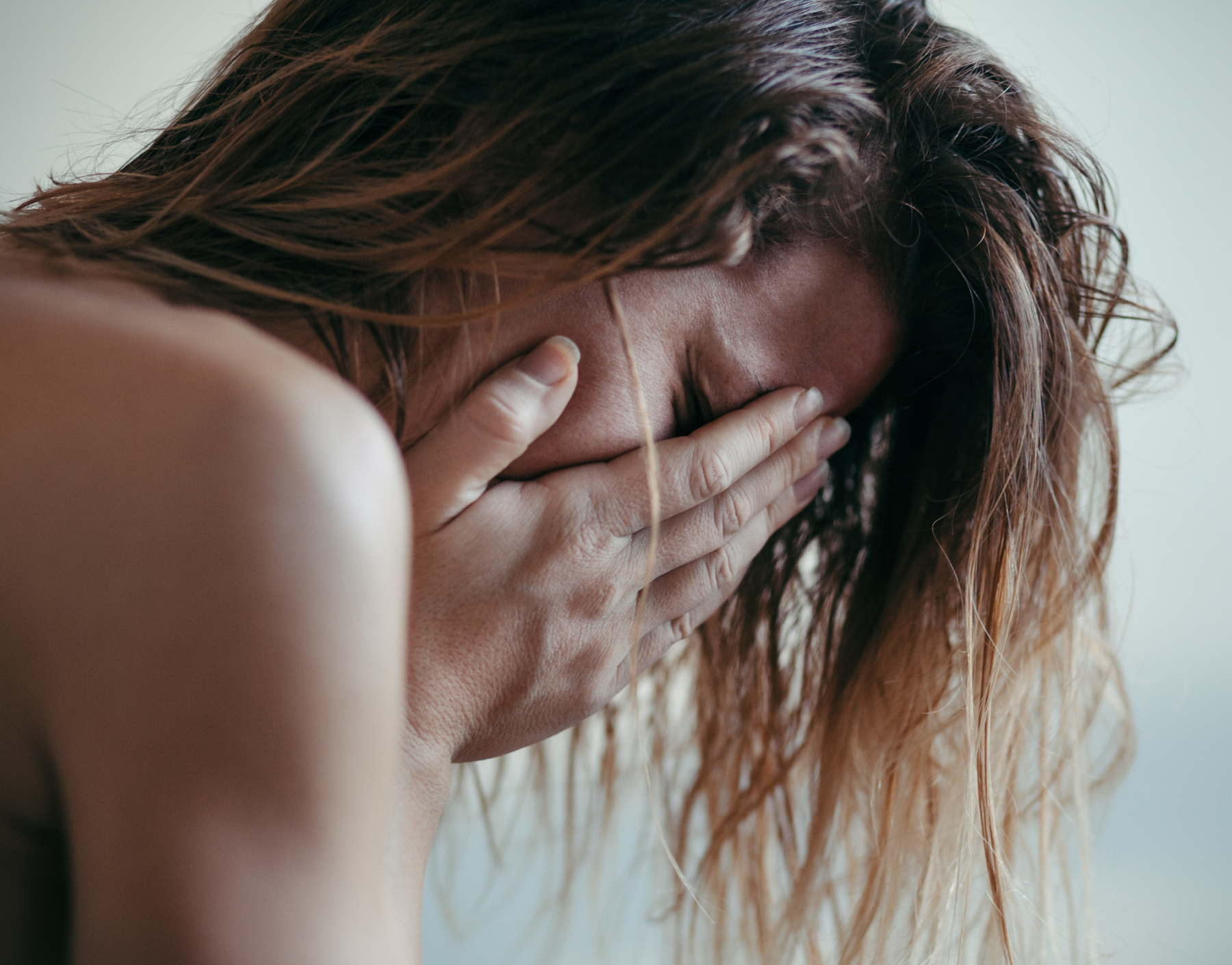 Person with long hair covering face with hands.