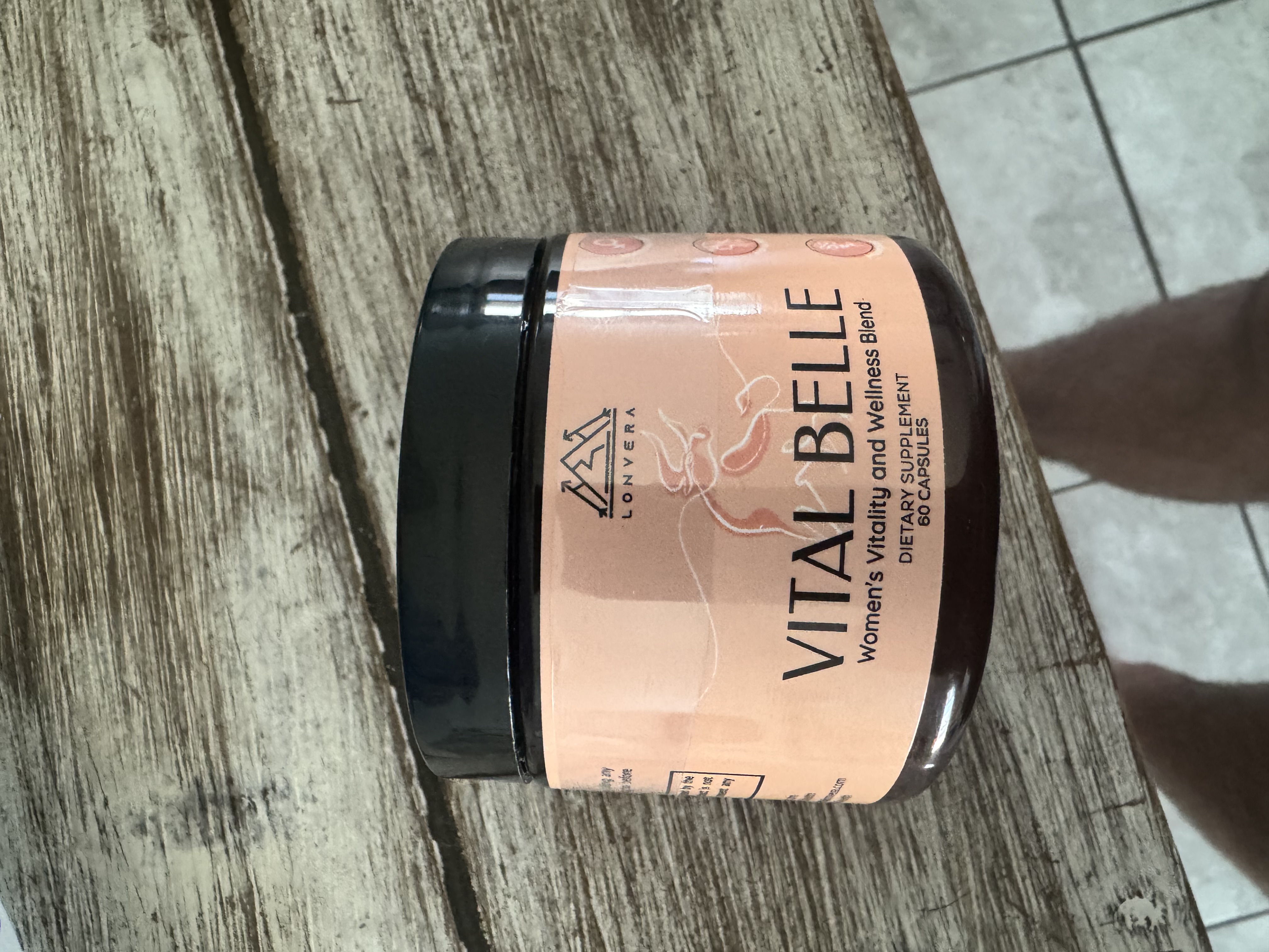 A jar of Vital Belle dietary supplement on a wooden surface.