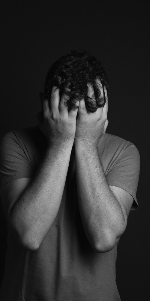 Person covering face with hands in a dark setting.