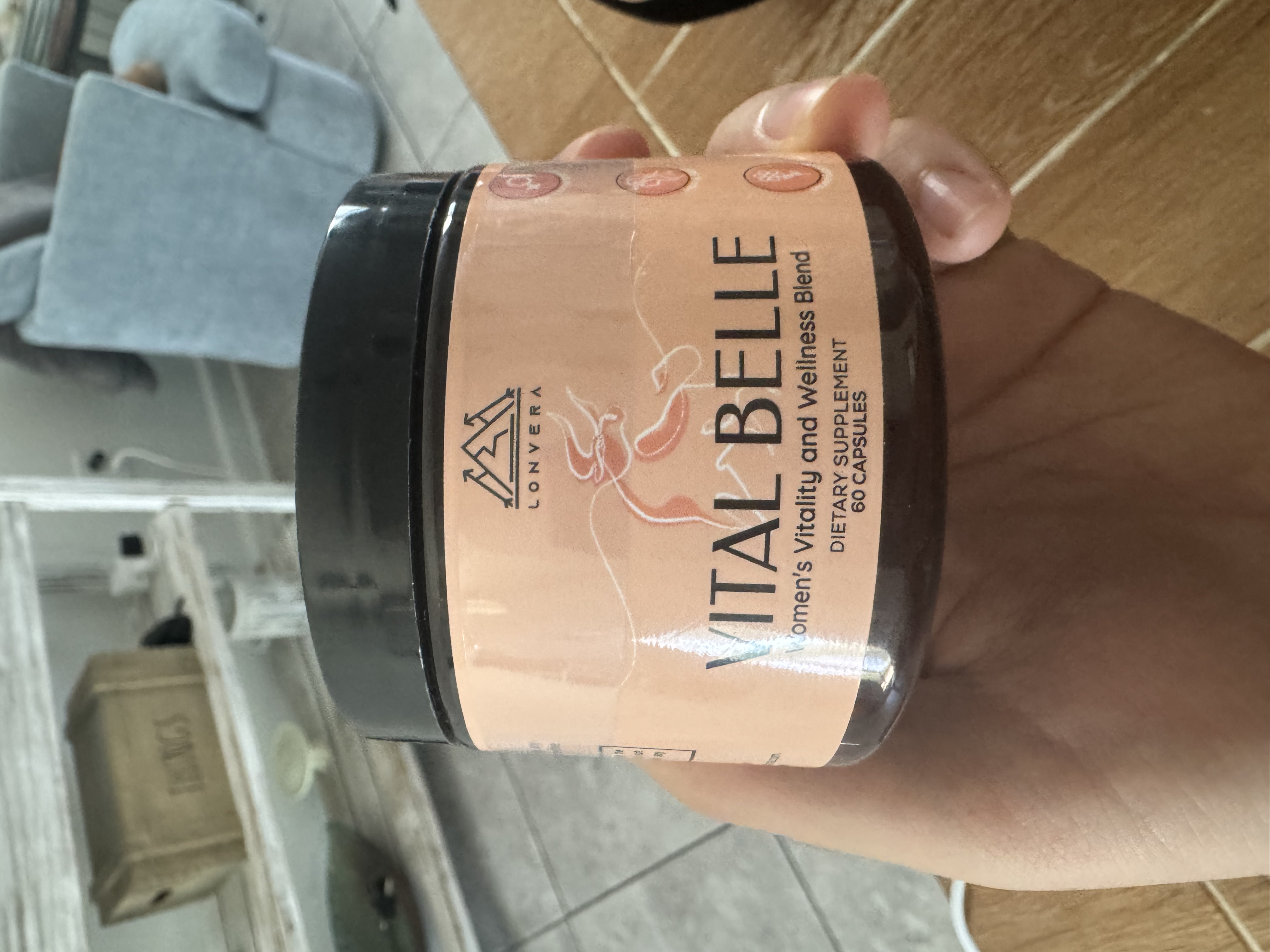 Hand holding a jar labeled 'Vital Belle' dietary supplement.