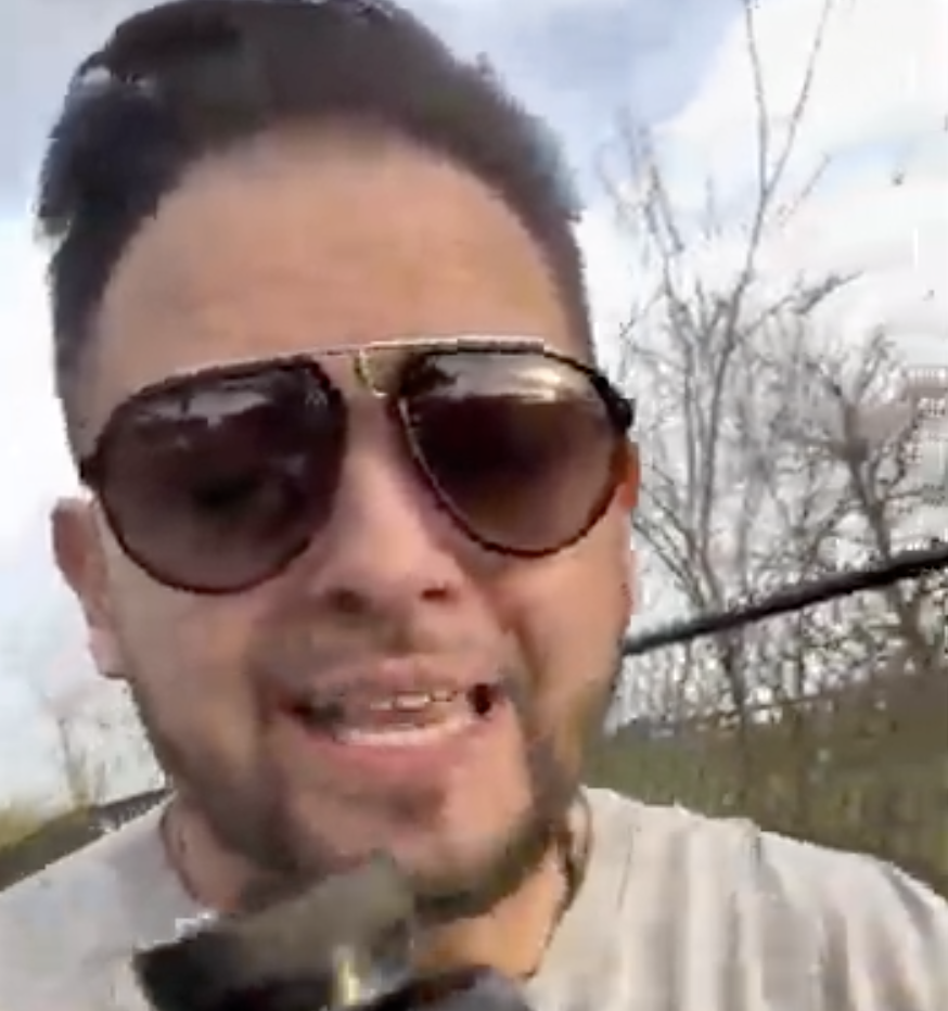 Person wearing sunglasses outdoors, holding a microphone.