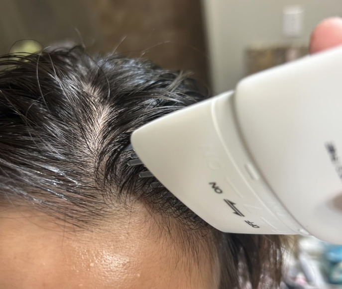 A close-up of a white comb applicator being used on a person's wet hair and scalp.