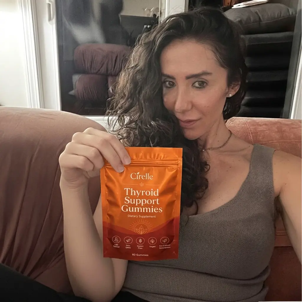 A woman with dark curly hair holds up a pouch of Cirelle Thyroid Support Gummies.