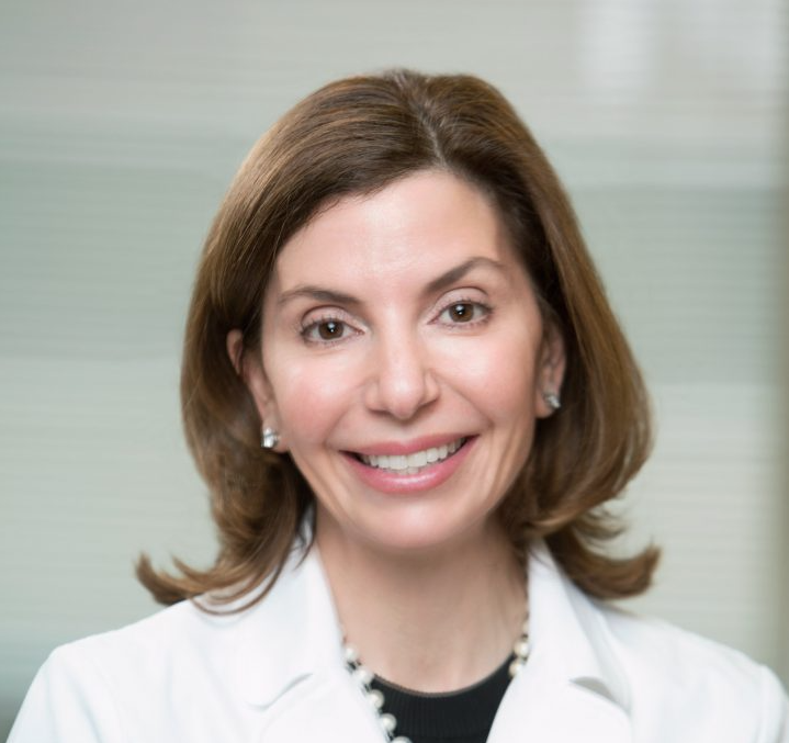 Smiling woman wearing a white coat and earrings.