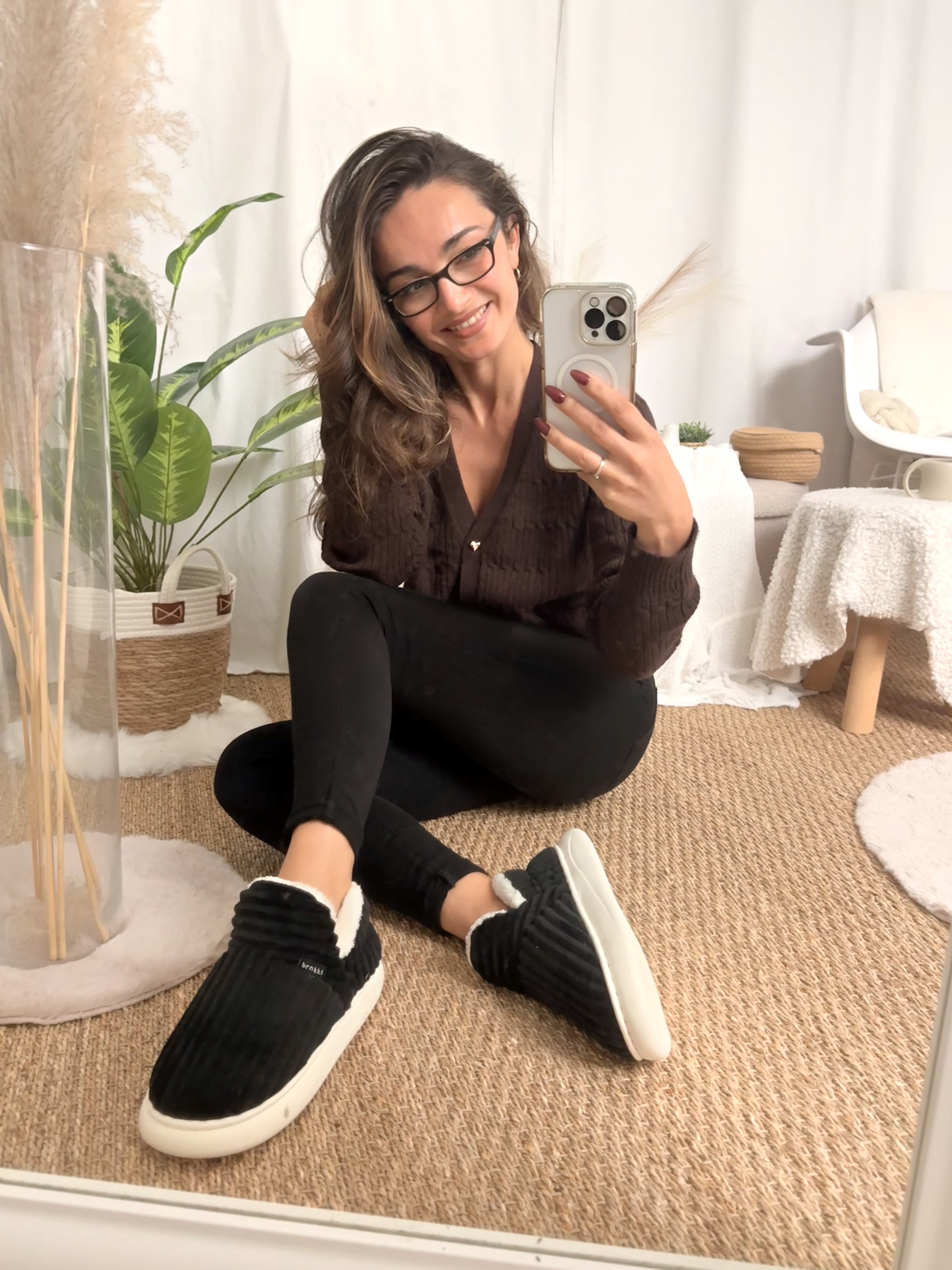 Person sitting on floor, taking a selfie in front of a mirror, surrounded by plants.