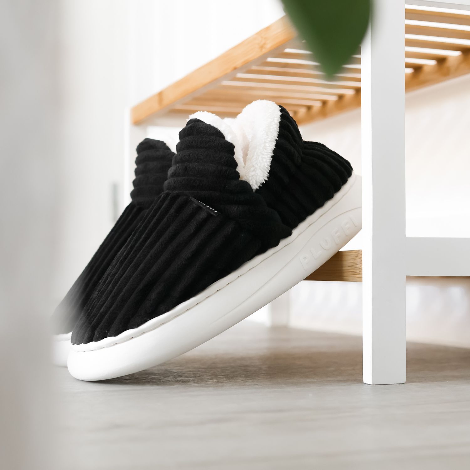 Black ribbed slippers with white soles and fleece lining under a wooden bench.