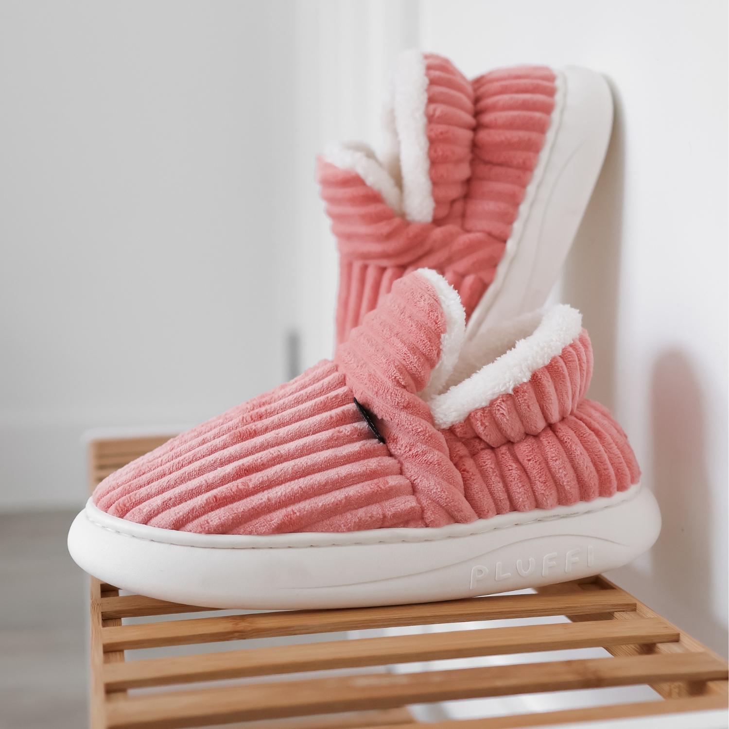 Pair of pink ribbed slippers with white soles on a wooden shelf.