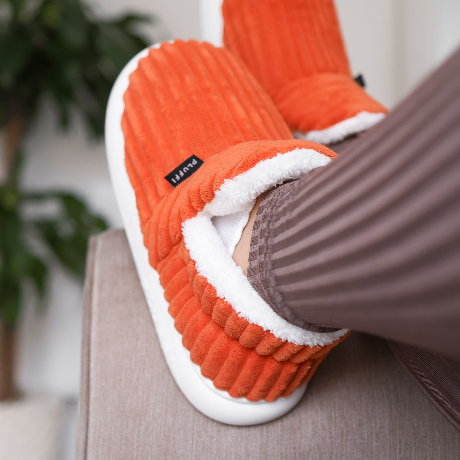 Pair of pink ribbed slippers with white soles on a wooden shelf.