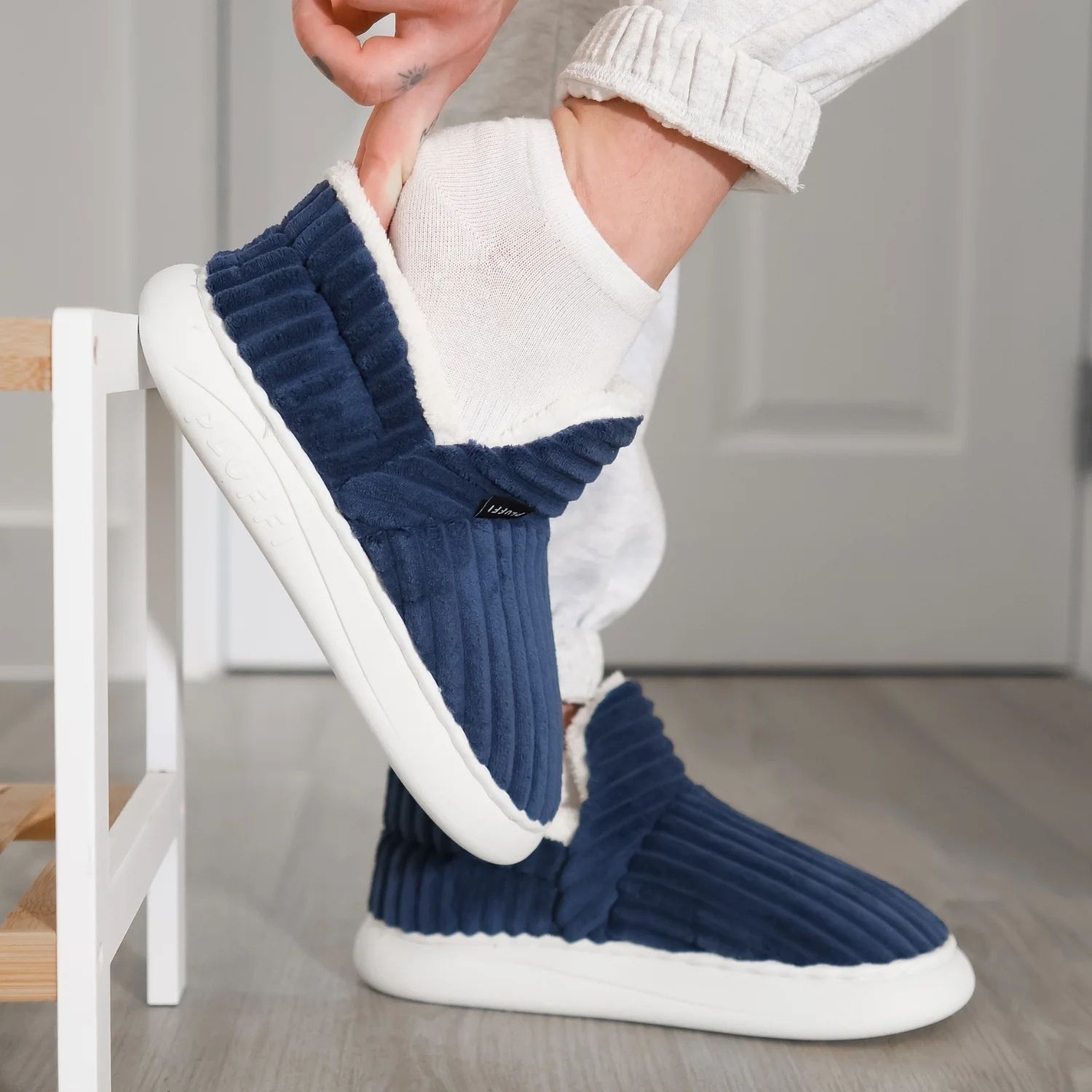 Person wearing blue slipper with white socks indoors.