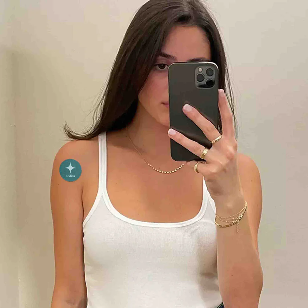 Person taking a mirror selfie with a smartphone, wearing a white tank top.