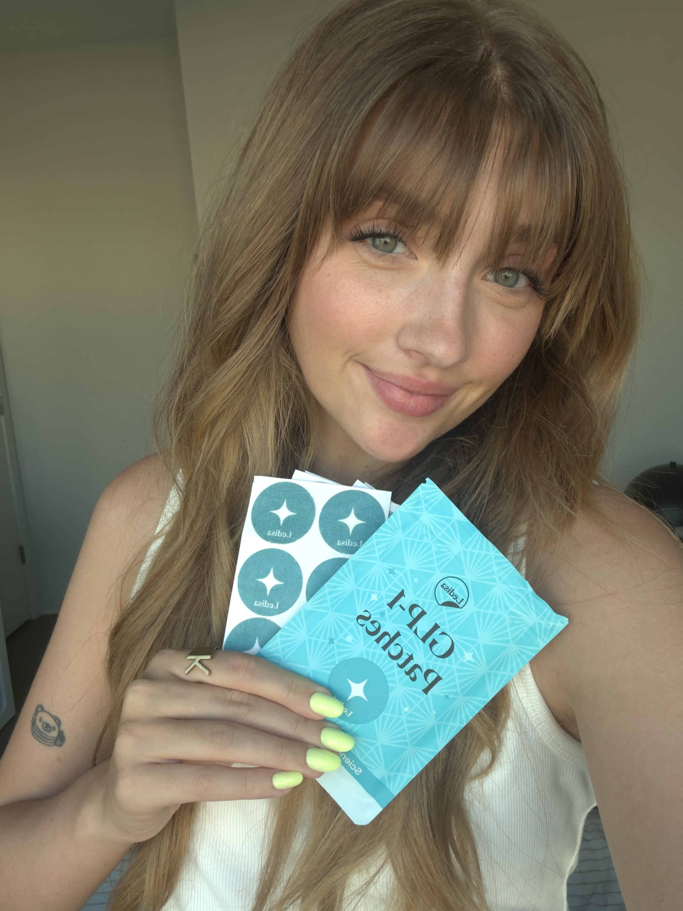 Person holding skincare product packets, smiling, with long hair and light green nails.