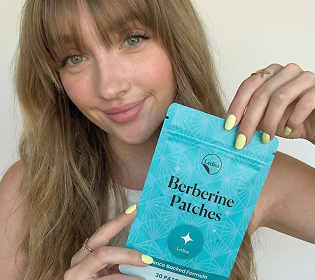 A woman with blonde hair holds a blue pouch of Ledisa Berberine Patches while smiling at the camera.