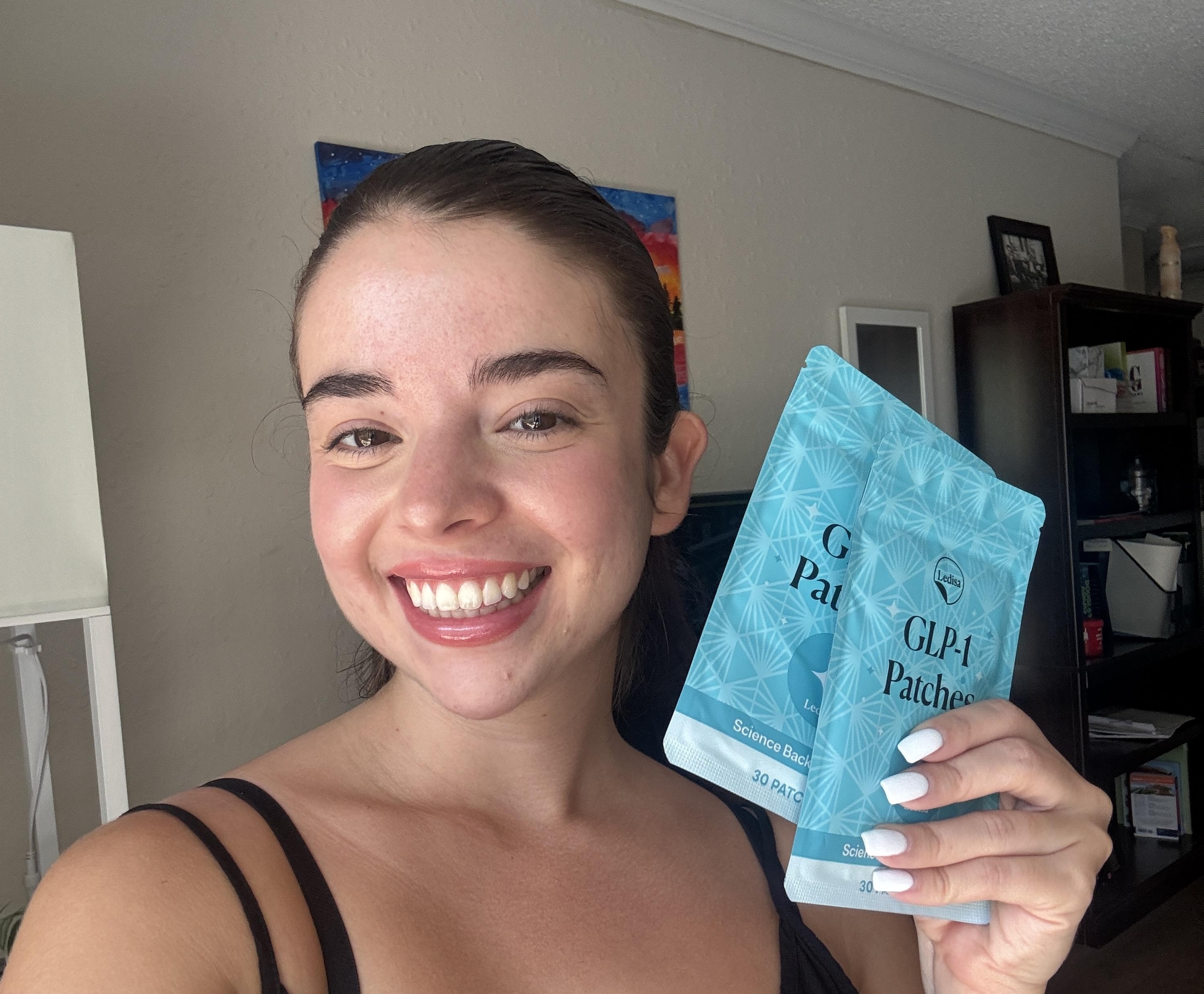 Person smiling and holding GLP-1 patches in a room.