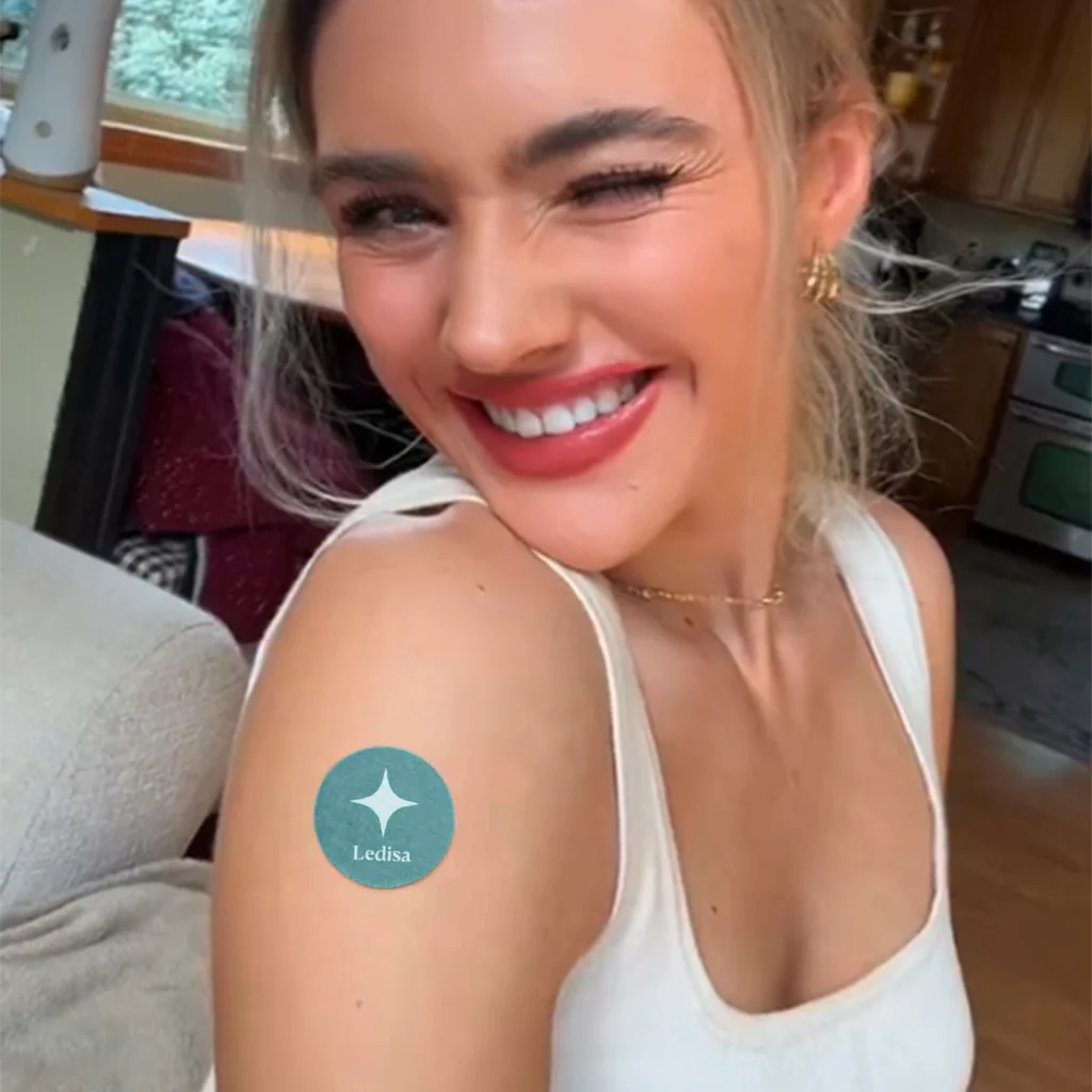 Smiling person winking, wearing a white top, indoors.